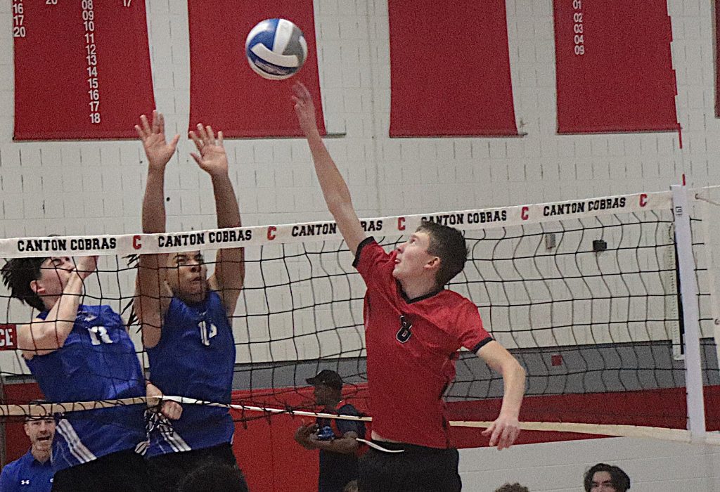 Indoor volleyball game at Canton Cobras gym; players in blue and red jump to reach the ball at the net.