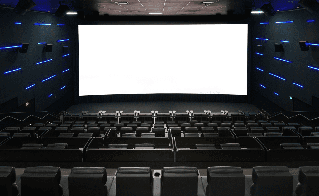 Empty modern cinema with a large white screen, dark walls, and blue LED strips along the sides above the seats.
