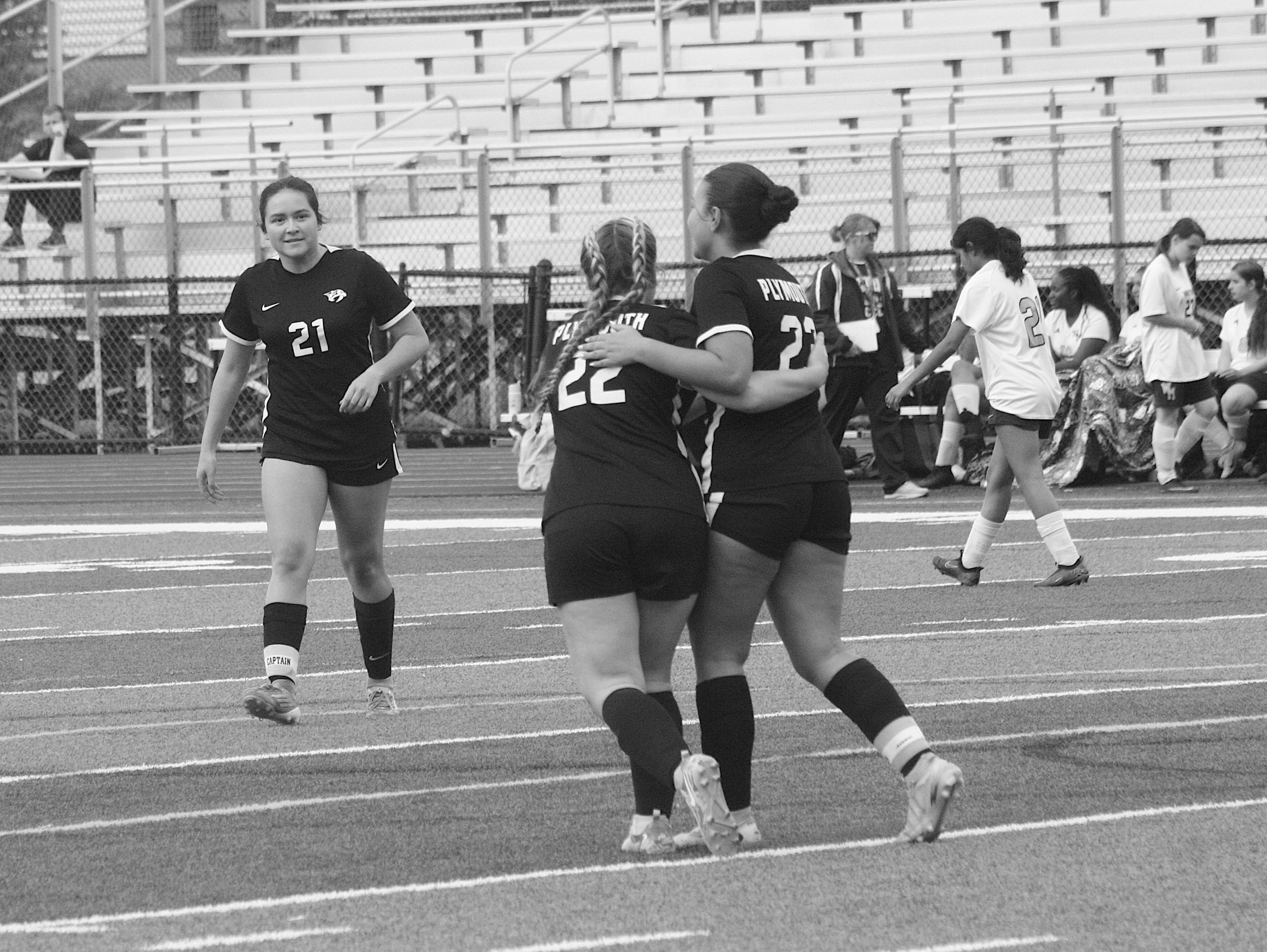 Catszebs1 - Social House News Girls' soccer teammates in black uniforms celebrate with arms around each other on a track beside bleachers after a game.
