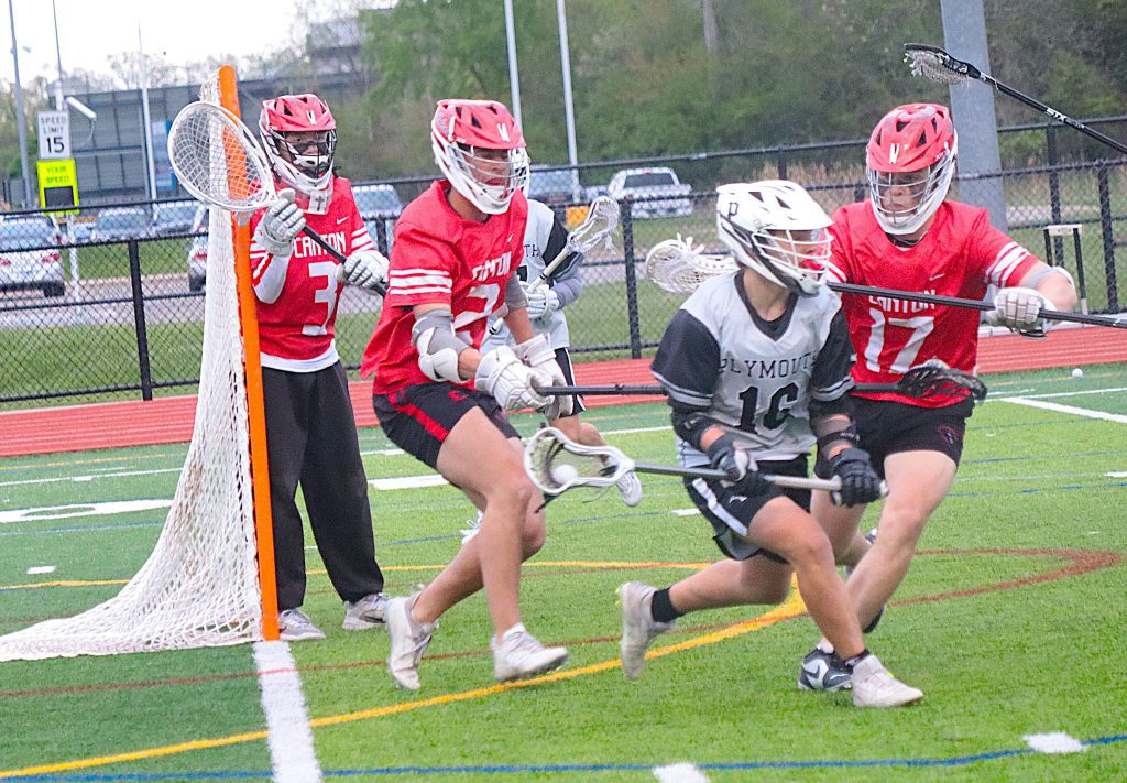 Lacrosse players collide near the goal crease as a goalie guards the net in red and gray uniforms.