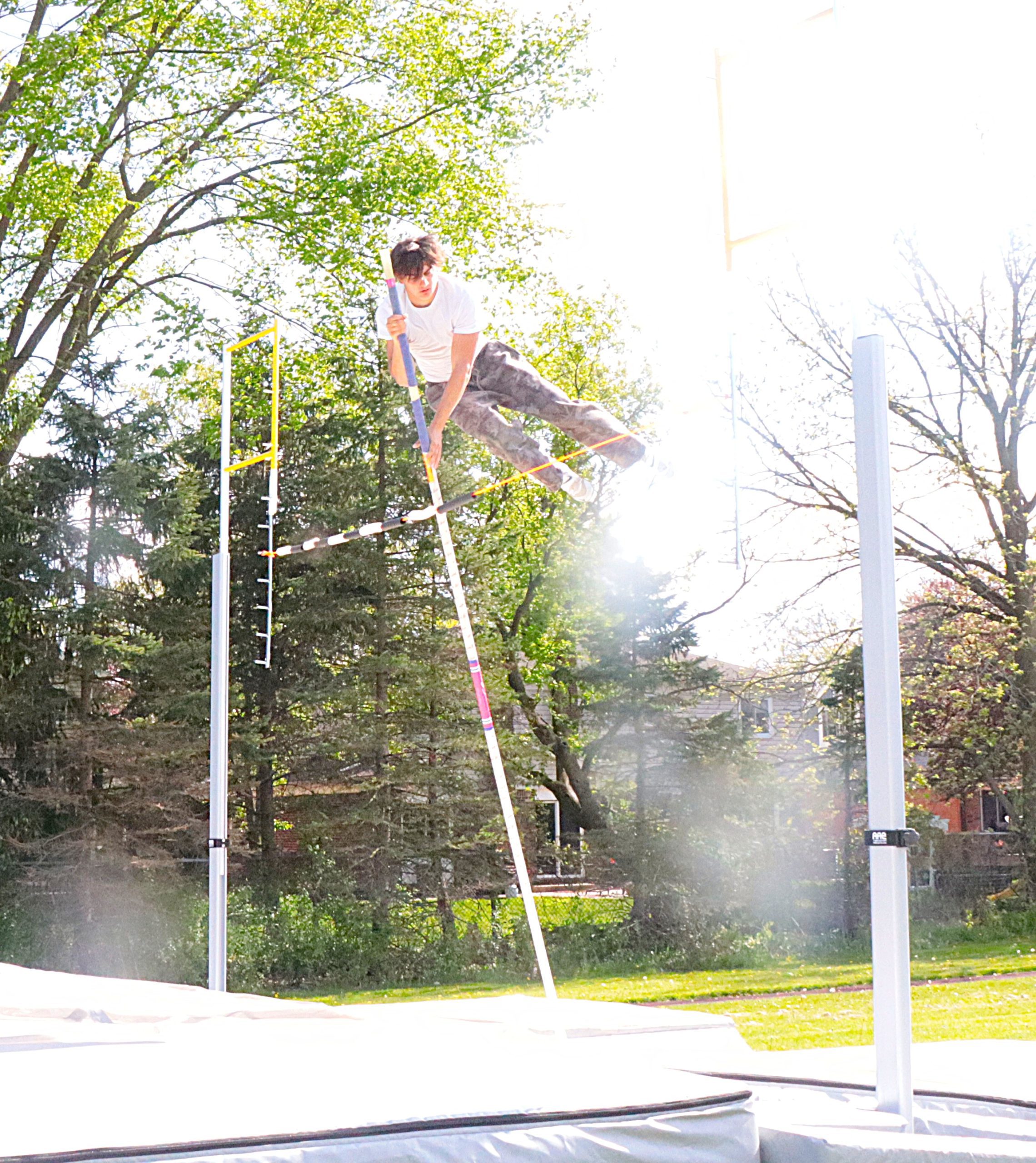 Man in a white shirt balancing on a raised slackline between poles in a sunny park setting.