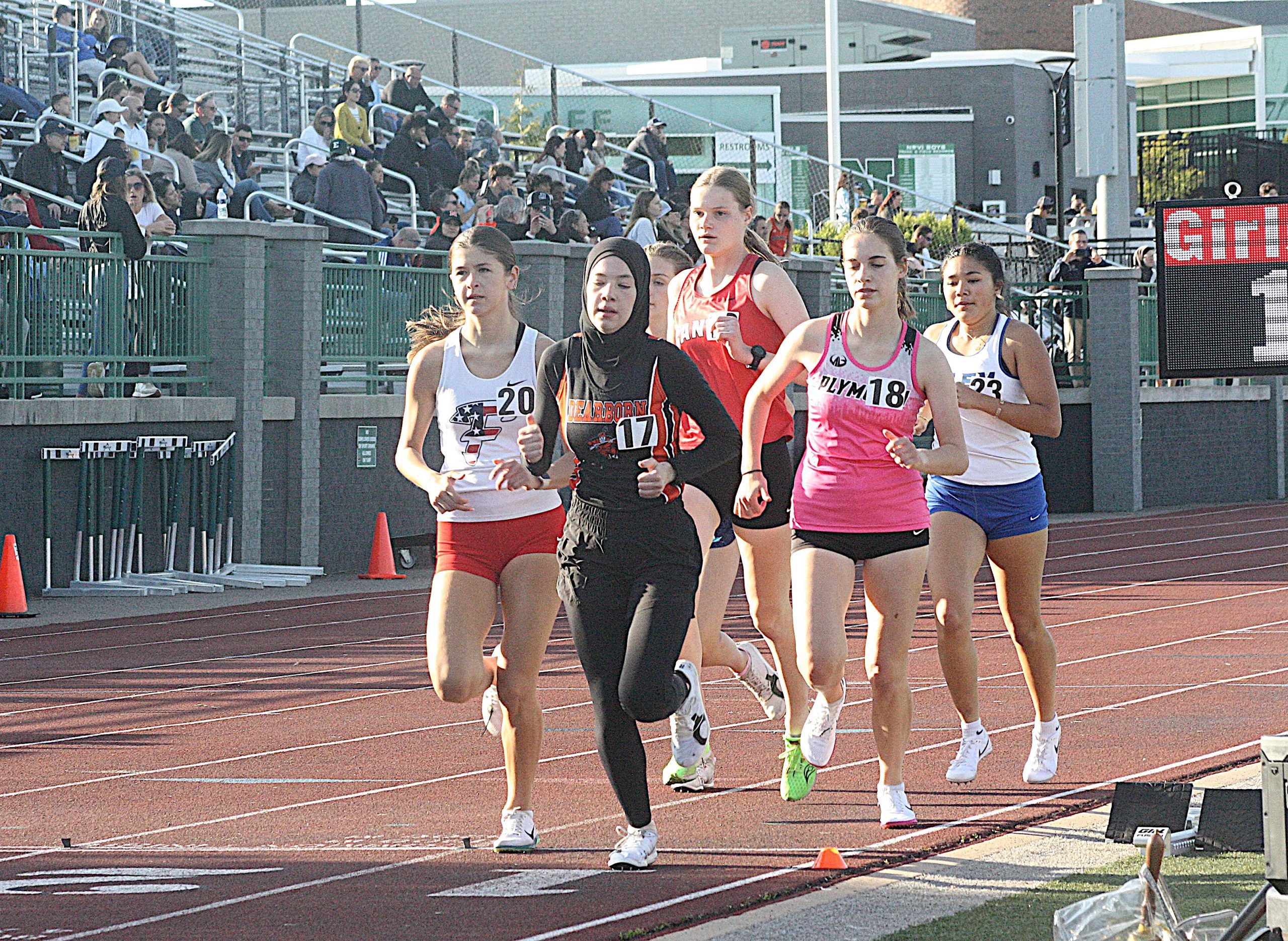 tfreg6 - Social House News Group of female runners on a red track during a race, with spectators in the stands behind them.