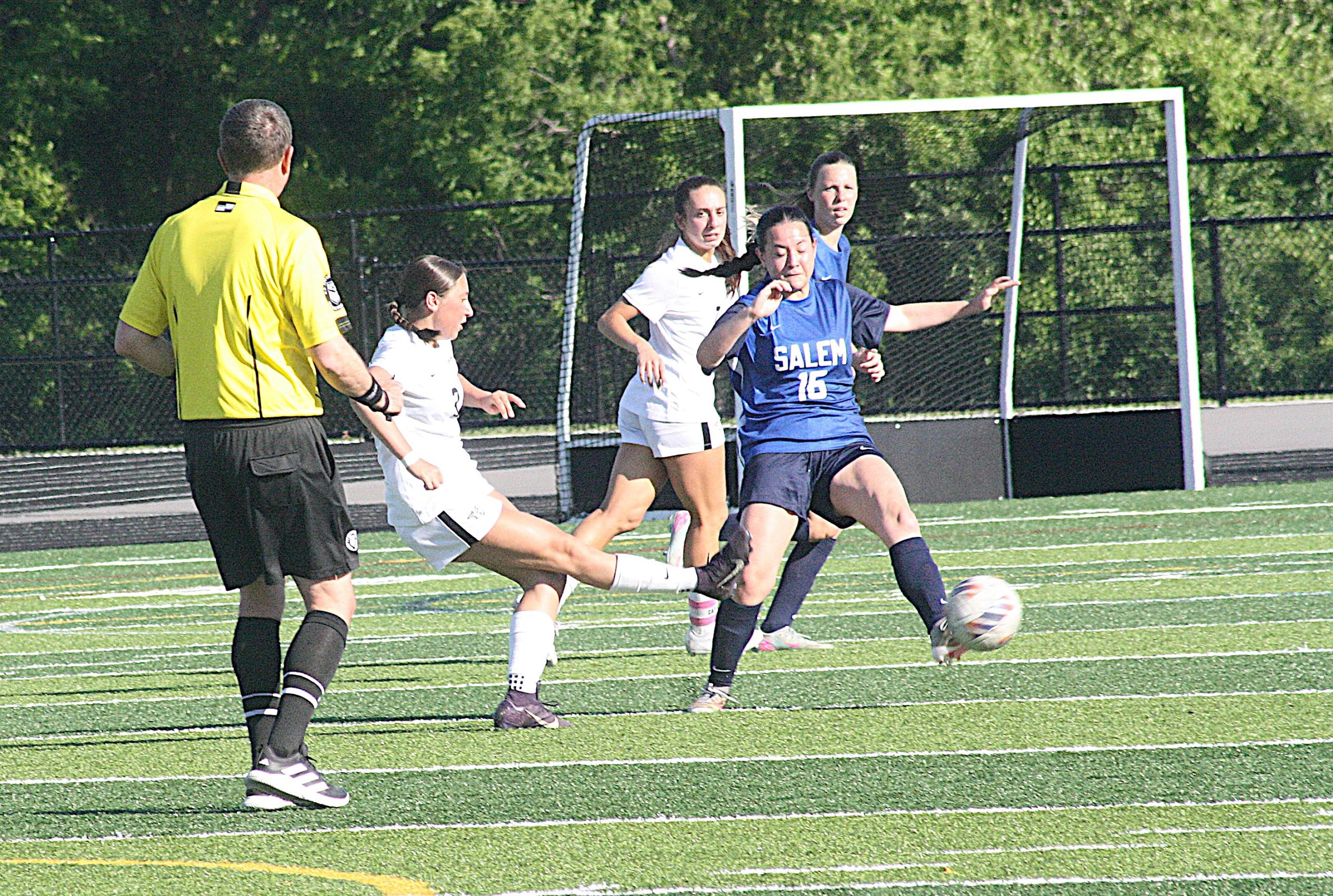 Girls' soccer game: blue Salem #16 controls the ball as white-team players close in near the goal, referee in yellow on left.