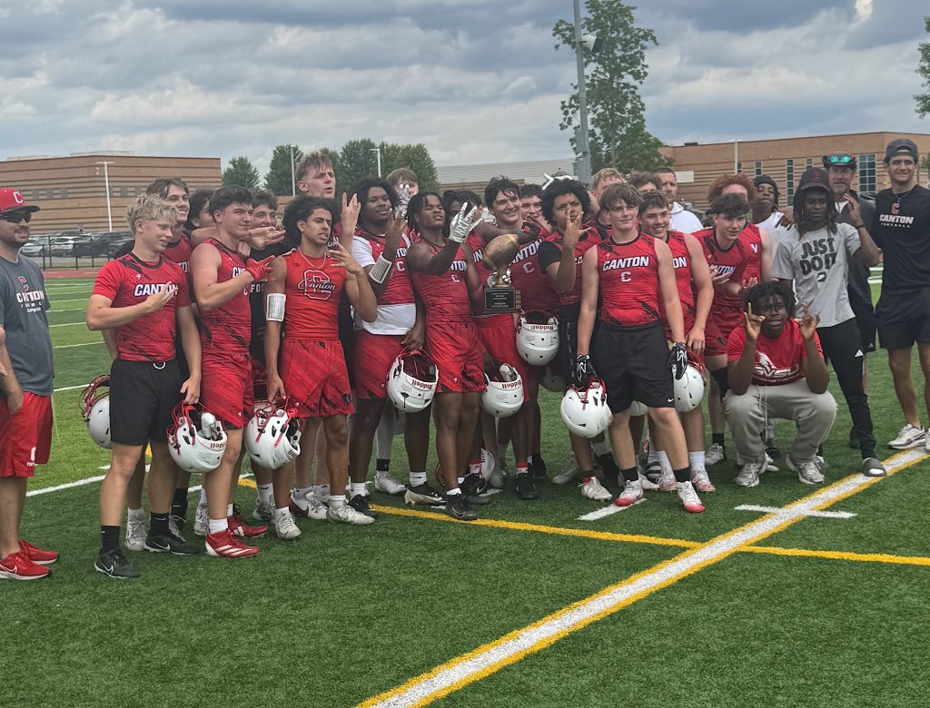 Youth football team posing on a field with helmets off, proudly displaying a trophy.