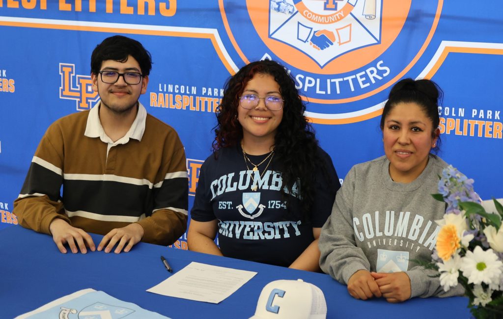 Three students sit at a blue signing table in front of a Railsplitters banner, smiling at the camera.