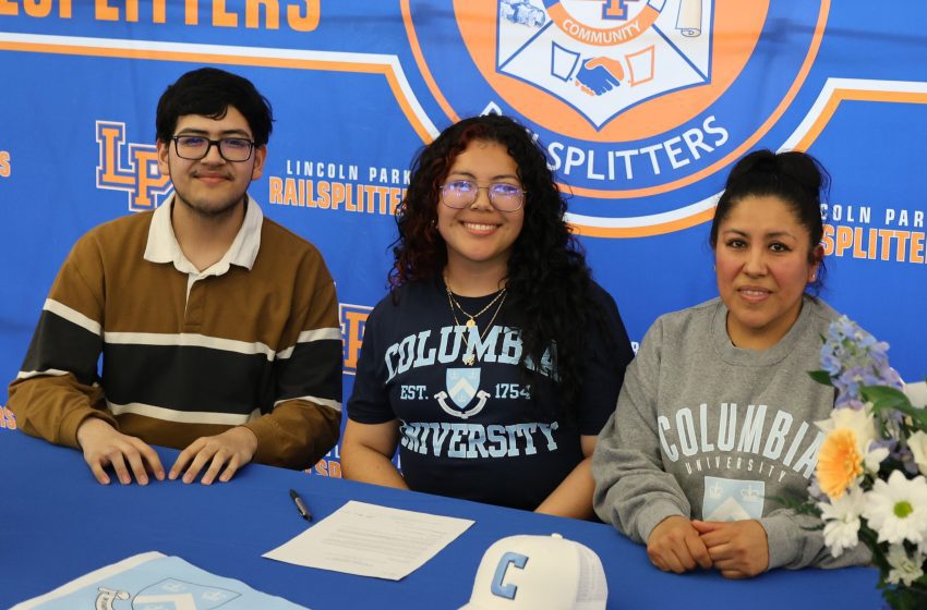 Three students sit at a blue signing table in front of a Railsplitters banner, smiling at the camera.