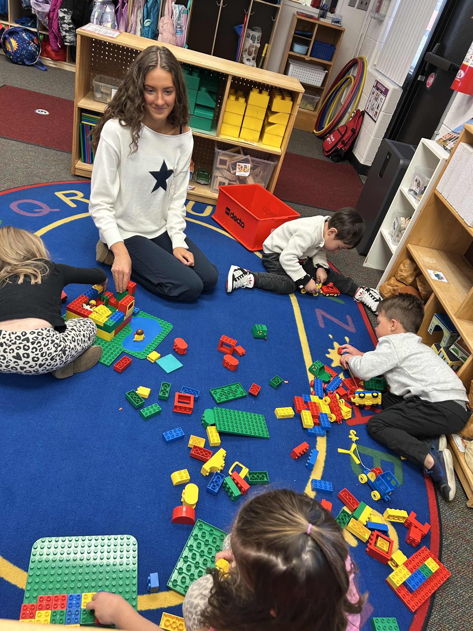 FutureTeachers3 - Social House News Group of children building with colorful LEGO bricks on a blue classroom rug.