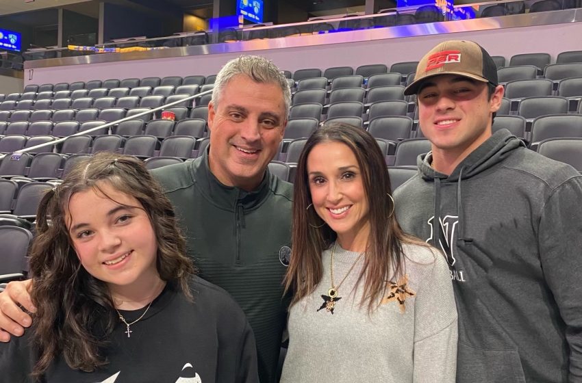 Four people pose together in a mostly empty stadium seating area, smiling at the camera.