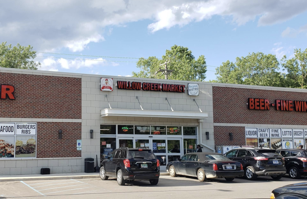 Willow Creek Market storefront with red sign, brick exterior, and several parked cars in front.