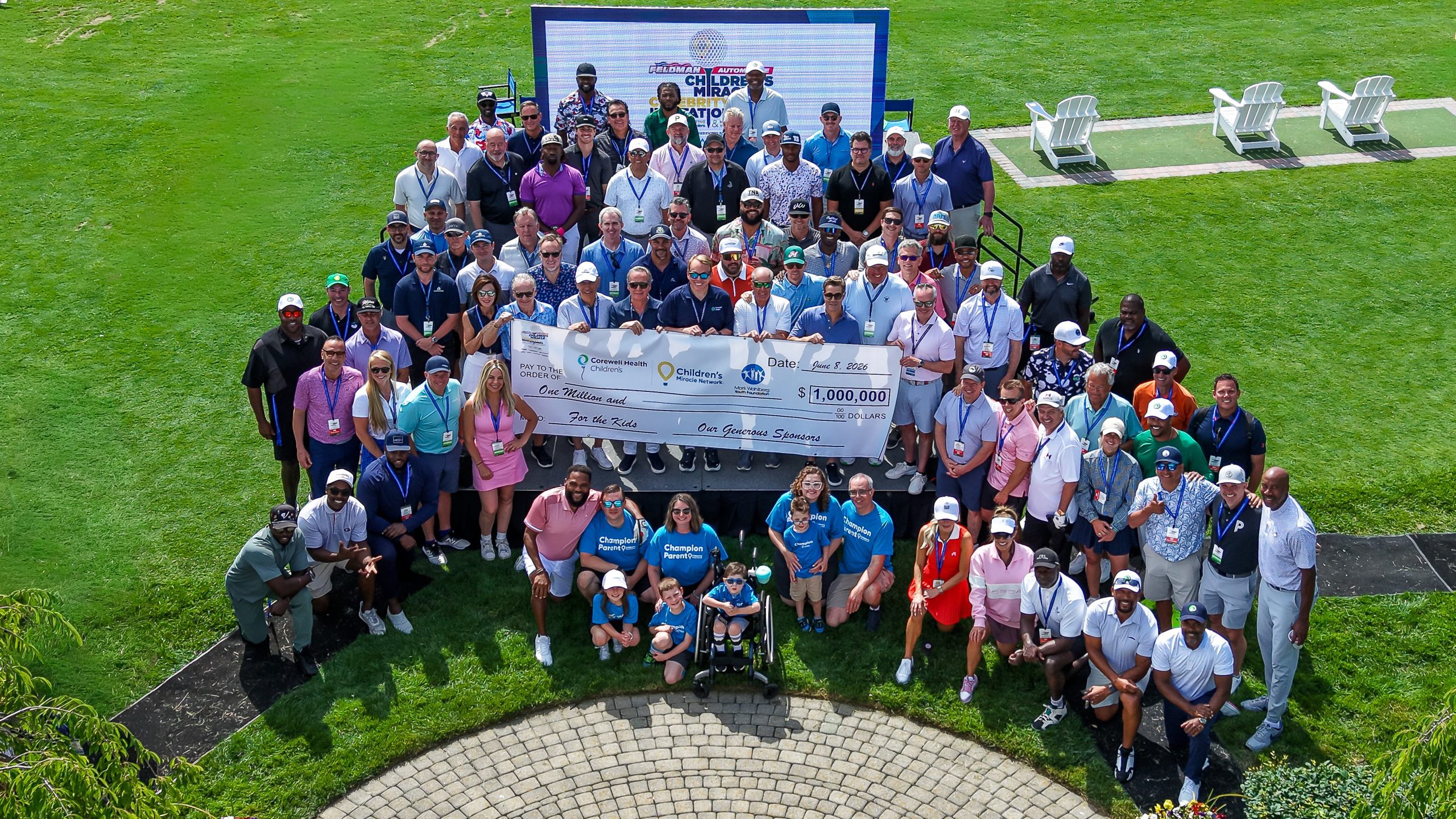 Feldman Golf Outing - Social House News Large group of people on a grassy field posing with a giant ceremonial check at an outdoor event.