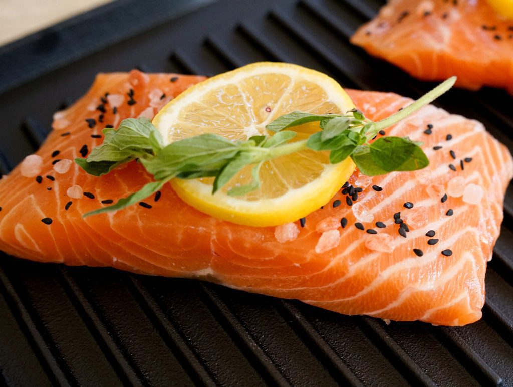 Salmon fillets on a grill garnished with a lemon slice, fresh herbs, and black sesame seeds