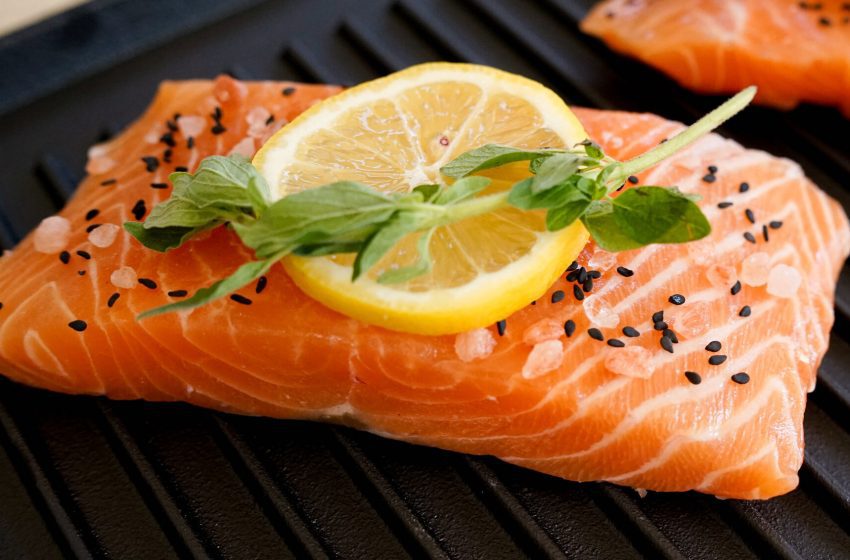 Salmon fillets on a grill garnished with a lemon slice, fresh herbs, and black sesame seeds