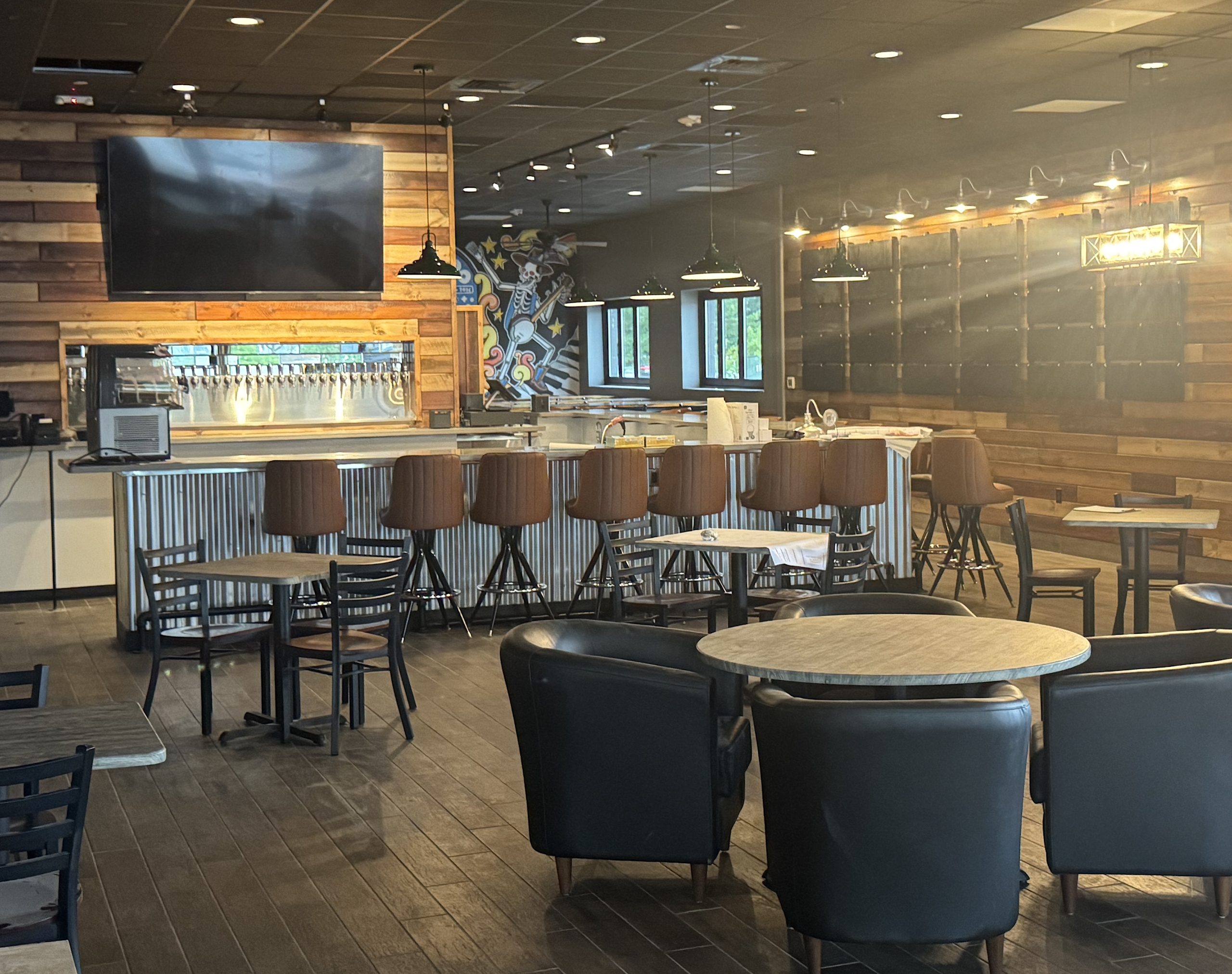 Voodoo3 - Social House News Modern bar area with wooden paneled walls, brown bar stools, and round tables under hanging lights.
