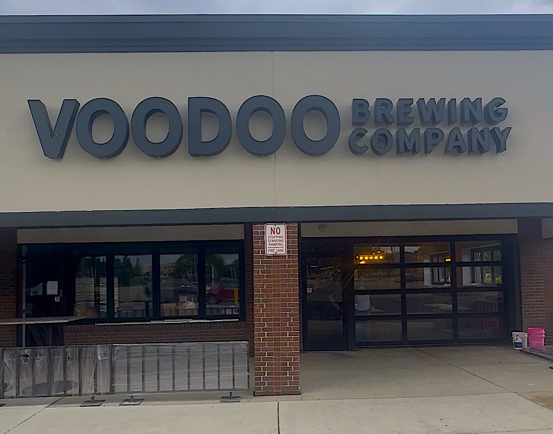 Screenshot - Social House News Front of Voodoo Brewing Company storefront with large blue letters on a pale wall and brick pillar at the entrance.