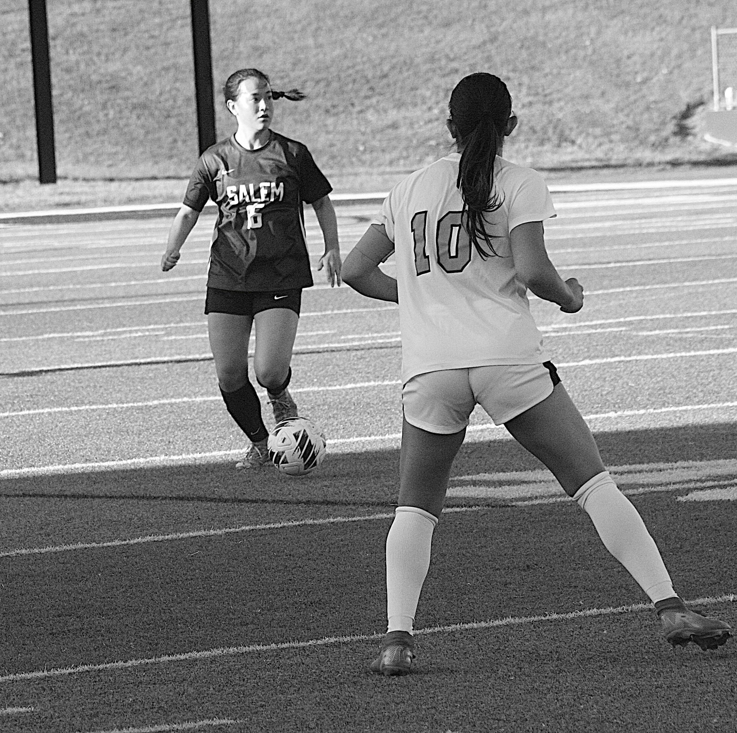 Two female soccer players compete for the ball on a field; one in a dark Salem jersey (number 16) faces an opposing player in a light jersey (number 10).