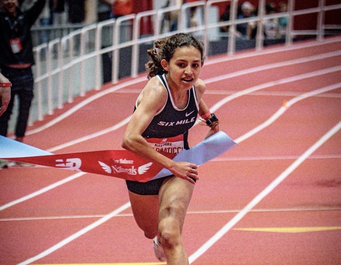 Screenshot - Social House News Female sprinter crosses the finish line on a red track, wearing a black Six Mile singlet.
