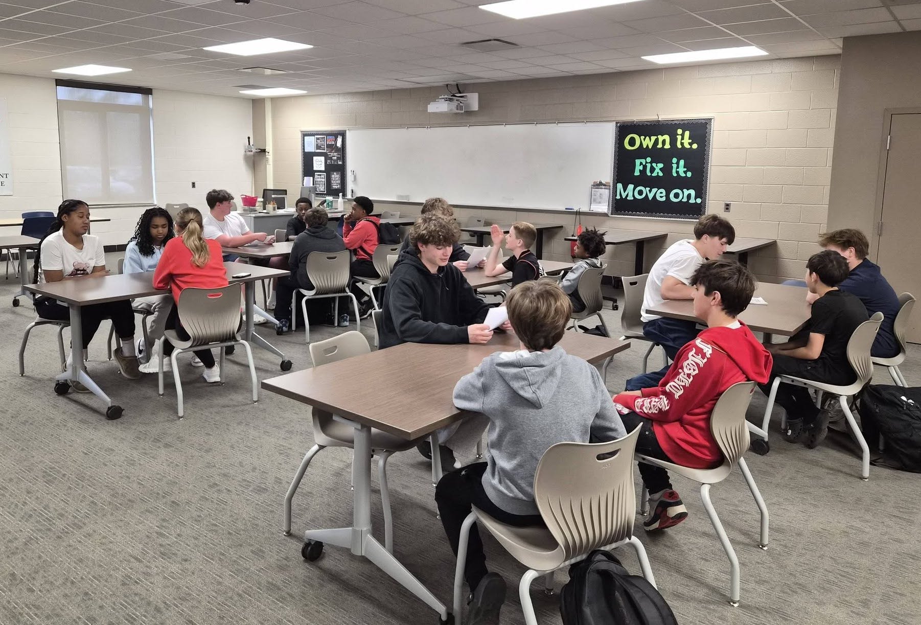 CHS Mentors 3 - Social House News Classroom with students in small groups at tables, collaborating; banner on wall reads 'Own it. Fix it. Move on.'