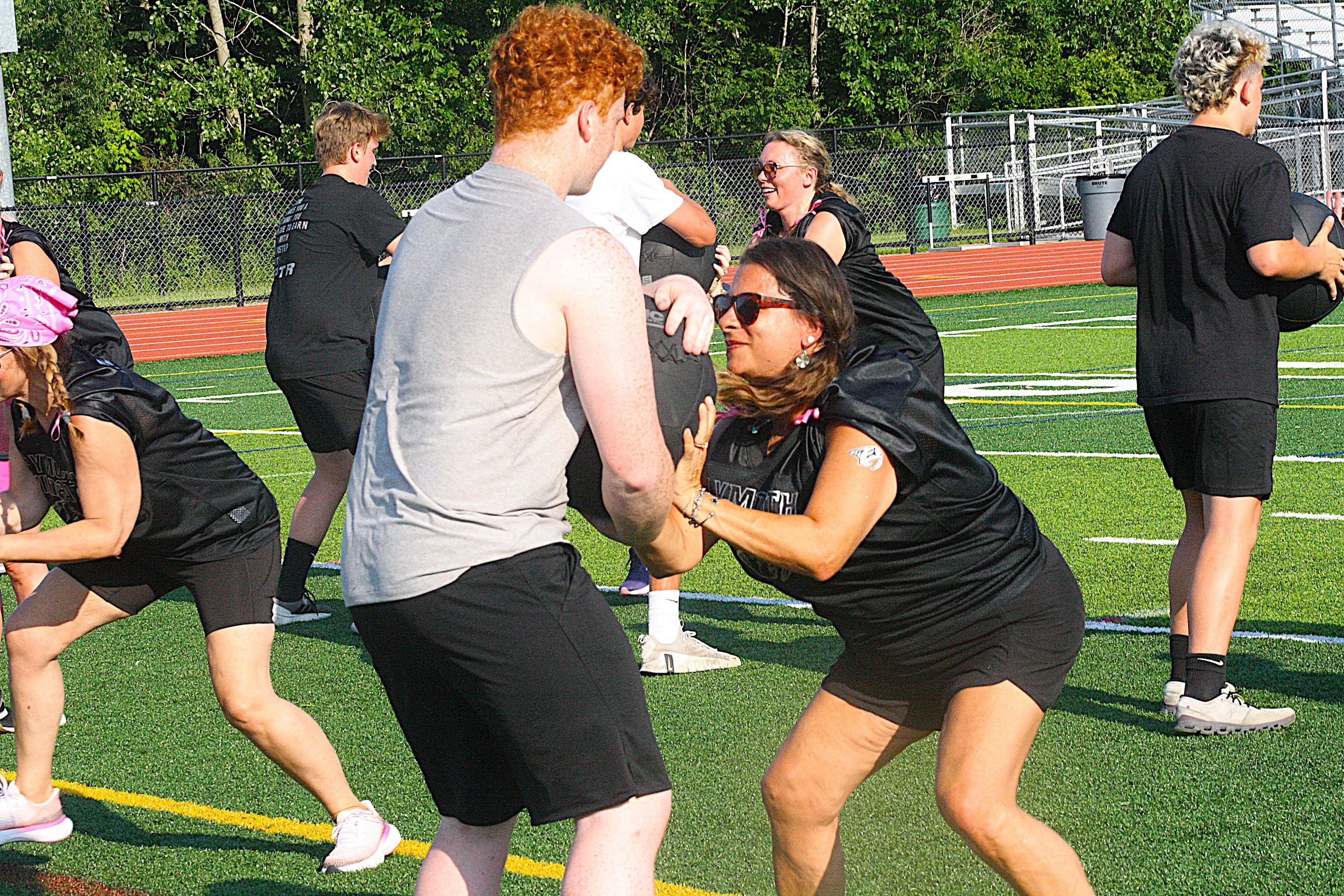 People playing flag football on a synthetic turf field, wearing black and gray uniforms, reaching for the ball and embracing.