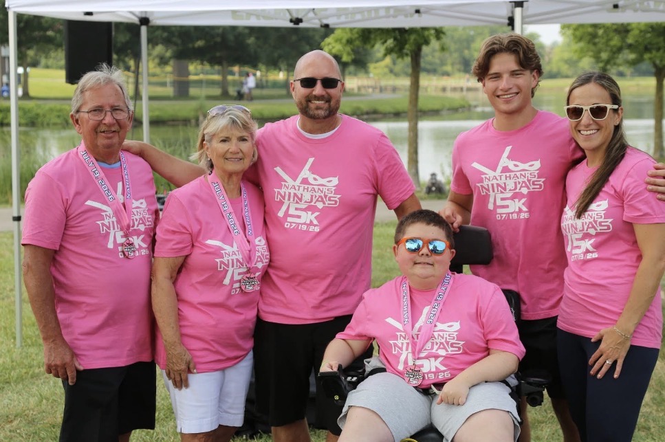 Screenshot - Social House News Group of six people wearing matching pink Nathan's Ninjas 5K shirts posing outdoors, smiling at the camera.
