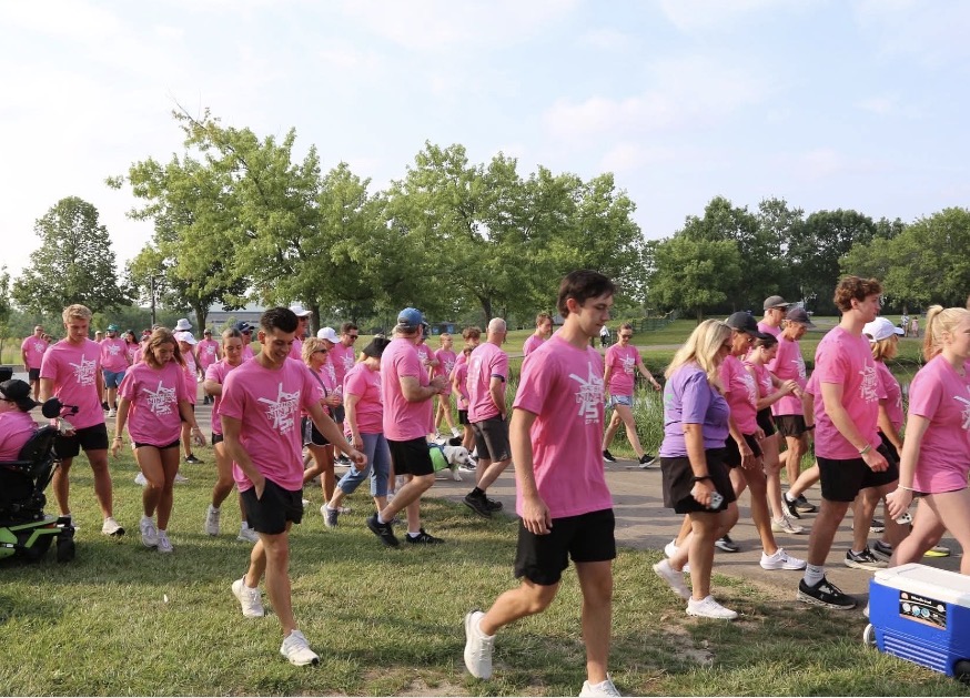 Screenshot - Social House News Group of people wearing pink shirts walking together in a park during a charity event.