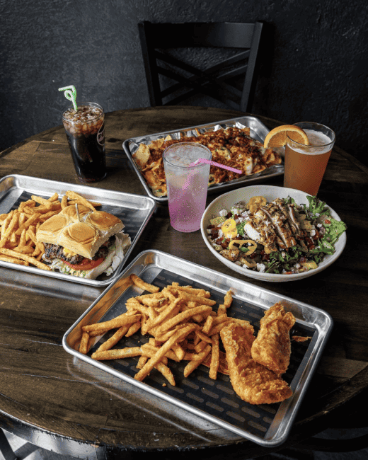 Tray of assorted fast-food dishes (burger, fries, fried chicken, salad) and drinks on a wooden table, shown as an Instagram post image with a caption area on the right.