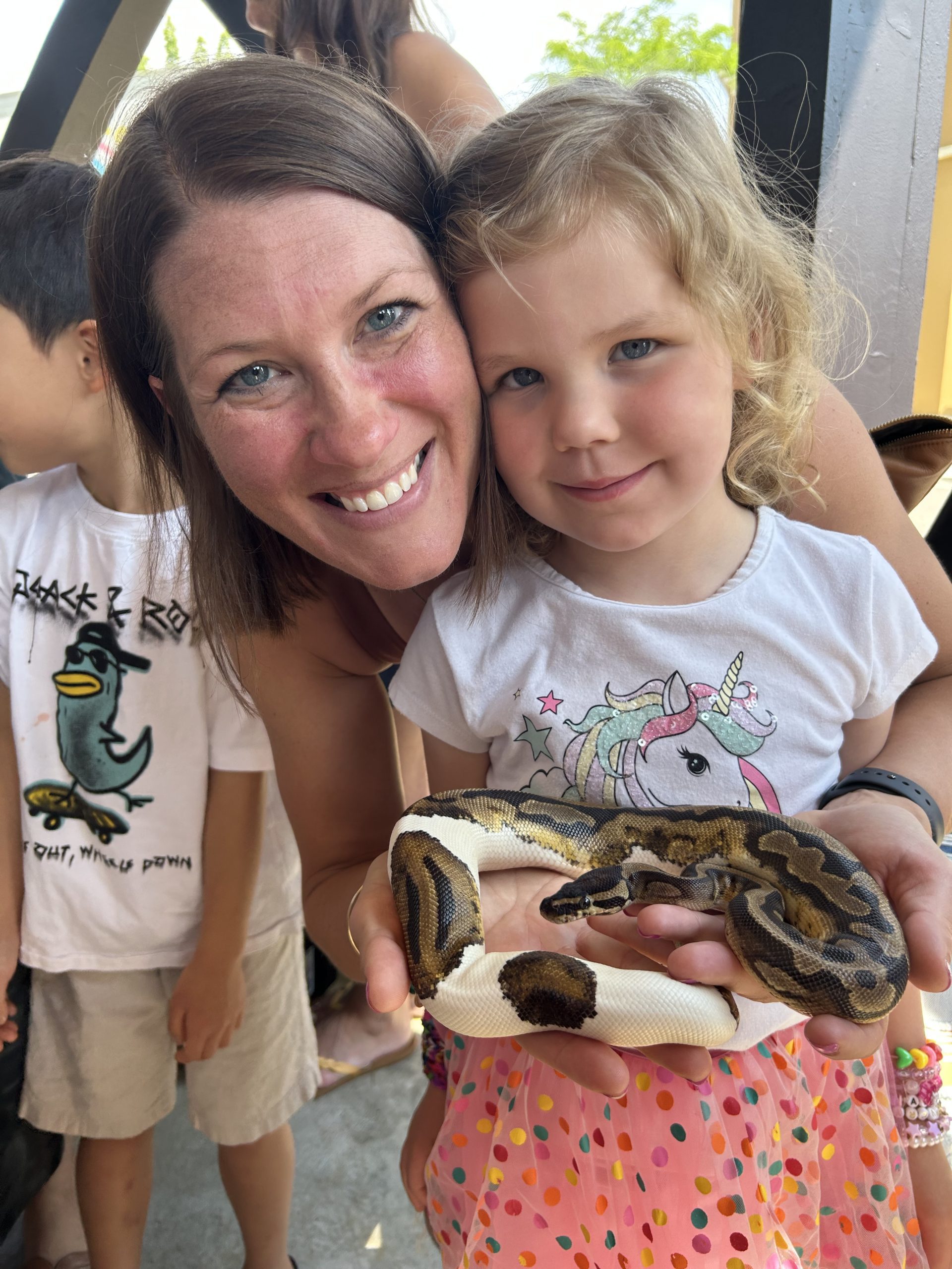 Smiling woman and young girl holding a brown and cream snake outdoors.