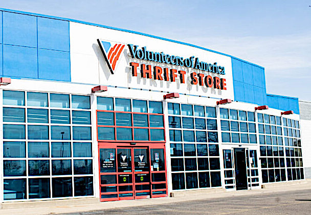 Front of Volunteers of America Thrift Store, blue building with large glass windows and red entrance doors, sign above says VOLUNTEERS OF AMERICA THRIFT STORE